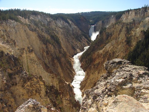 Foto von einem Fluss der durch eine steinige Schlucht führt. Im Hintergrund sieht man einen Wasserfall. Das Foto wurde an dem 'Grand Canyon of the Yellowstone' aufgenommen.