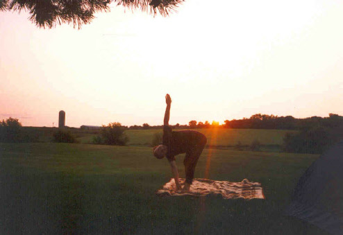 Christian beim Yoga auf einer Decke vor einem roten Sonnenuntergang mit einem Silo im Hintergrund.